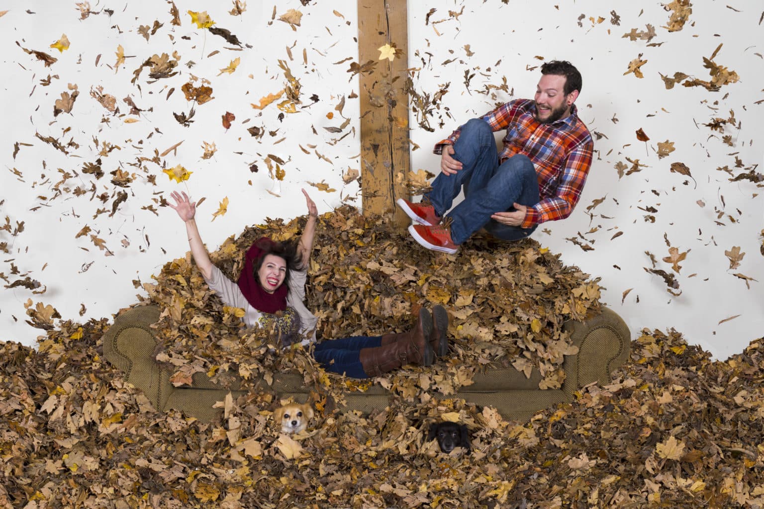 Lauren and Deven jumping through autumn leaves around the couch.