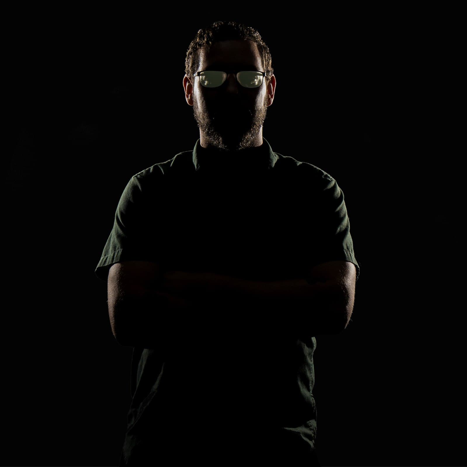 Low-key photographic portrait of Deven James Langston wearing glasses against a dark background.